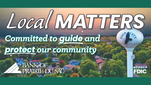 Aerial view of Sauk City at sunset with homes and water tower prominent. Text reads: Local Matters. Committed to guide and protect our community. Bank of Prairie du Sac. 